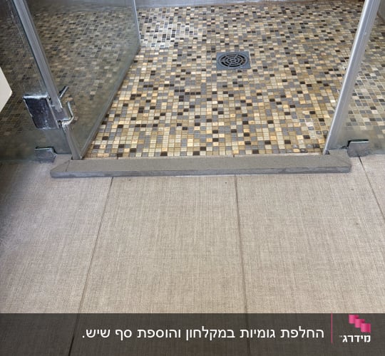 תקריב של סף מקלחון זכוכית עם דלת ציר ורצפת פסיפס